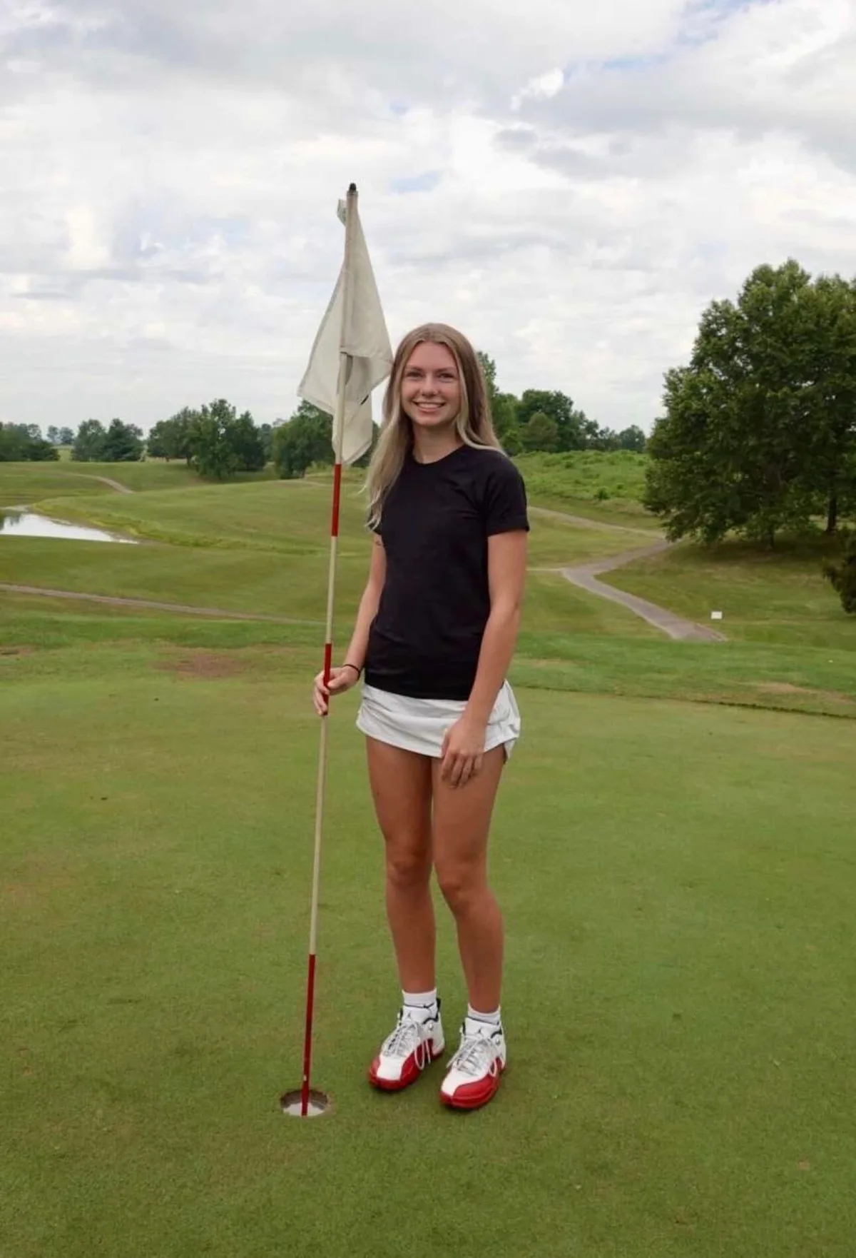 Ava Klips standing on a green holding the flagstick after a round