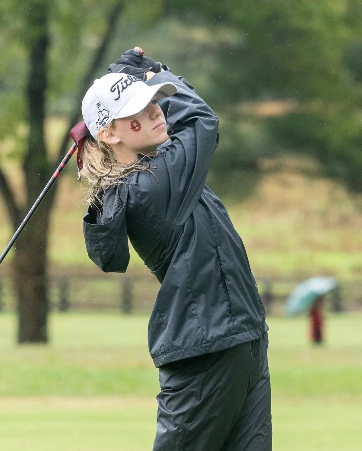 Ava Klips in black rain gear at the finish of a full swing in the rain