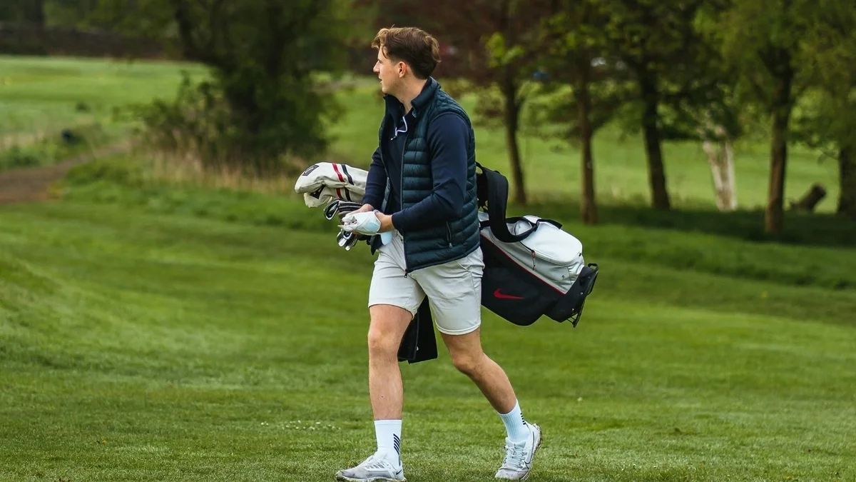 Golfer walking on course holding clubs and looking off after a shot